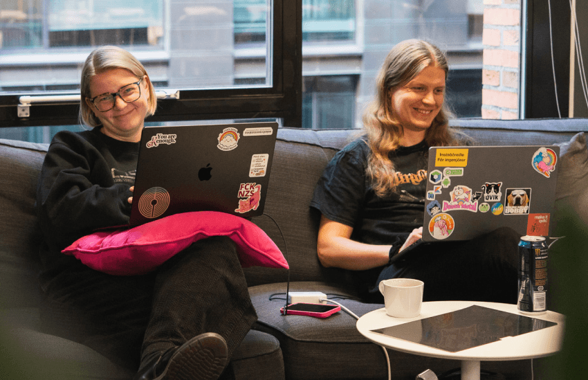 Kaksi kollegaa istuu sohvalla ja työskentelee kannettavilla tietokoneilla toimiston oleskelutilassa