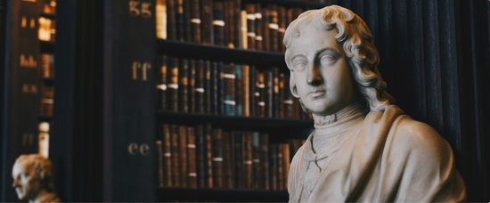 A white statue in front of a row of bookshelves with old books.