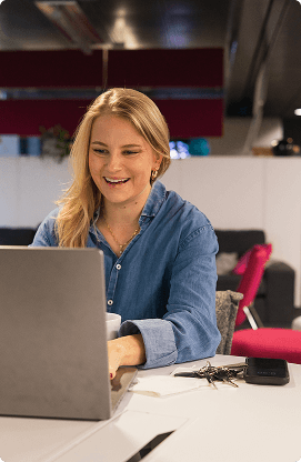 Tiimin tuotesuunnittelija istuu tietokoneen edessä ja hymyilee.